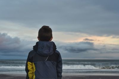 Rear view of man on beach against sky during sunset