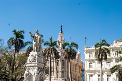 Low angle view of buildings and trees against clear blue sky