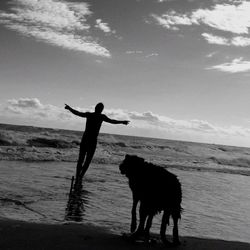 Silhouette man with dog standing on beach against sky