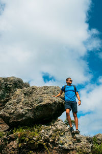 Low angle view of man standing on rock against sky