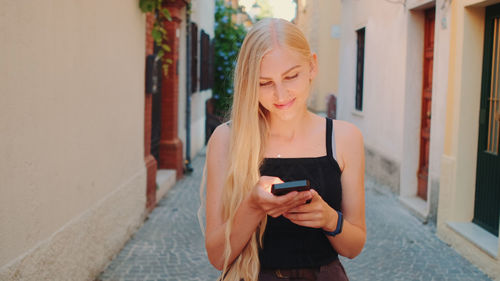 Young woman using mobile phone while standing on wall