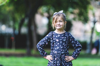 Portrait of cute smiling girl with arms akimbo standing in park