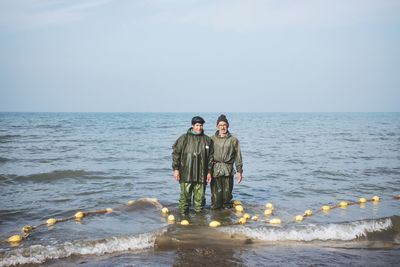 Men standing in sea against sky