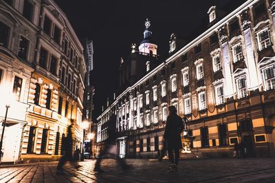 People walking on illuminated street amidst buildings at night