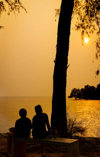 Silhouette people sitting by sea against sky during sunset