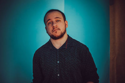 Portrait of young man standing against turquoise wall