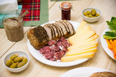 Plate of appetizers, sliced cheese, sausages, olives and nuts, bread with spices, jar of pate