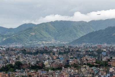 A view of the population density in city of kathmandu under a stormy sky with an airplane.