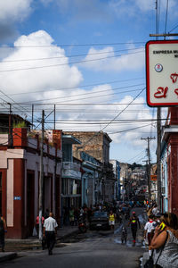 People walking on city street by buildings against sky