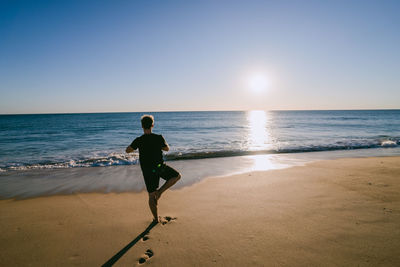 Rear view full length of man exercising at beach