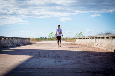 Portrait of teenage boy walking on road against sky