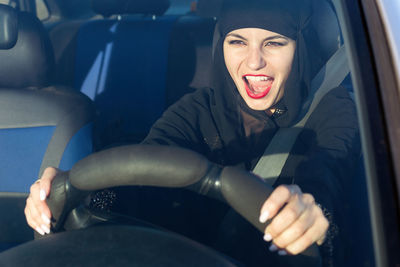 Woman wearing hijab screaming while driving car seen through windshield