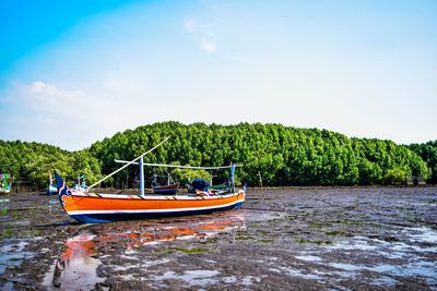 Boat moored on river by trees against sky