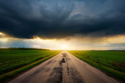 Road amidst field against sky during sunset