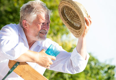 An elderly man sits sweating in the sun wearing a straw hat