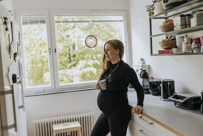 Pregnant woman holding cup in kitchen