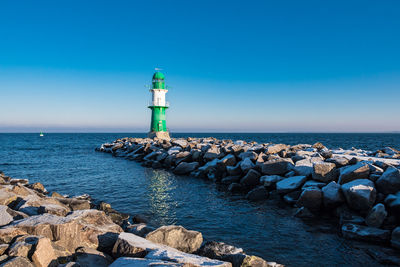 Lighthouse by sea against clear blue sky