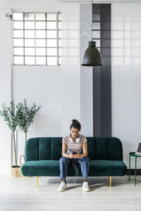 Female architect using smart phone while sitting on sofa at creative workplace