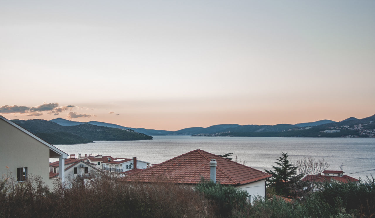 HOUSES BY SEA AND MOUNTAINS AGAINST SKY DURING SUNSET