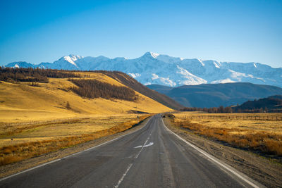 Road leading towards mountains against clear blue sky