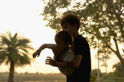 Side view of mother carrying daughter against sky