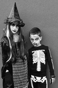 Portrait of girl and boy dressed in halloween costumes standing against wall