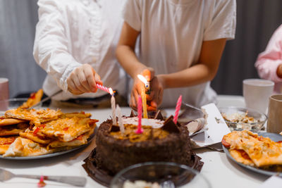 Midsection of people having food, children in white t-shirts lighting the birthday cake