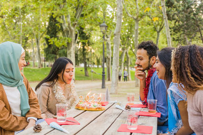 Friends toasting beer bottles while sitting at outdoor cafe