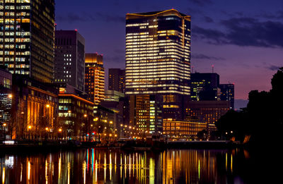 Illuminated buildings by river against sky at night