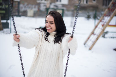 Smiling young woman swinging in snow covered playground