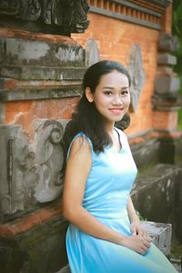 Portrait of smiling young woman sitting against old building