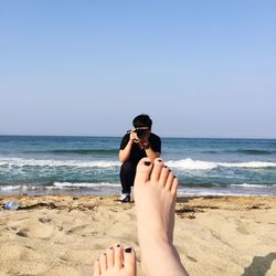 Man photographing woman leg on sandy beach