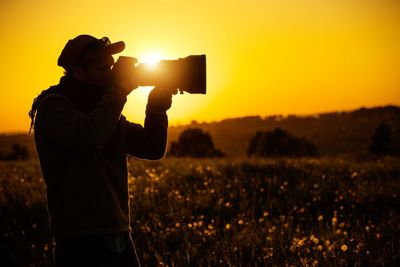 Silhouette man photographing on field against sky during sunset