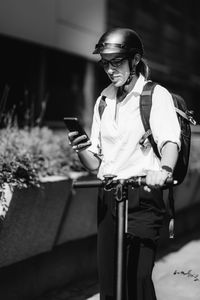 Businesswoman standing and using her smart phone with electric scooter next to her in the city.