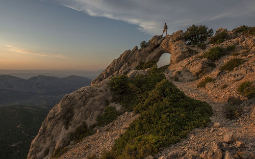 Scenic view of  man on natural arch against sky during sunset