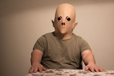 Man wearing alien mask while sitting at table against wall