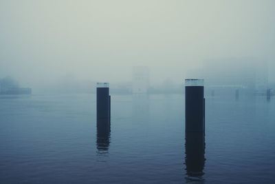 Wooden posts in sea against sky during foggy weather
