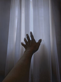 Close-up of hand against curtains at home