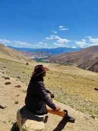 Side view of woman sitting on mountain against sky