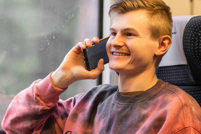 Young smiling man calling on smartphone when he traveling by train, using mobile phone, talking.