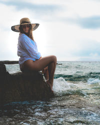 Young woman on rock at beach against sky