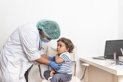 Paediatrician prepares infant vaccine for a blond caucasian child in a clinic.