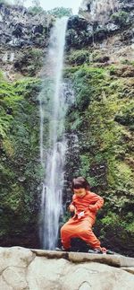 Woman sitting on rock by waterfall