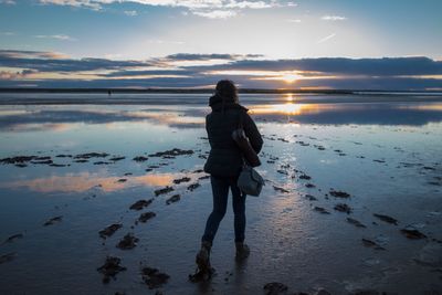 Rear view of woman walking at beach during sunset