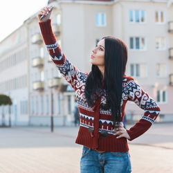 Young woman with arms raised standing in front of building