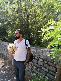 Man holding bouquet while standing by stone wall