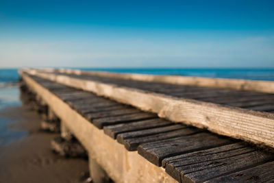 Close-up of wooden chairs at beach against blue sky