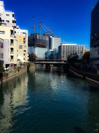 Buildings by canal against clear blue sky