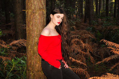 Portrait of young woman leaning on tree at forest