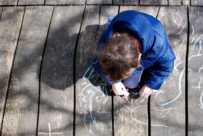 High angle view of boy drawing with chalk on wooden walkway